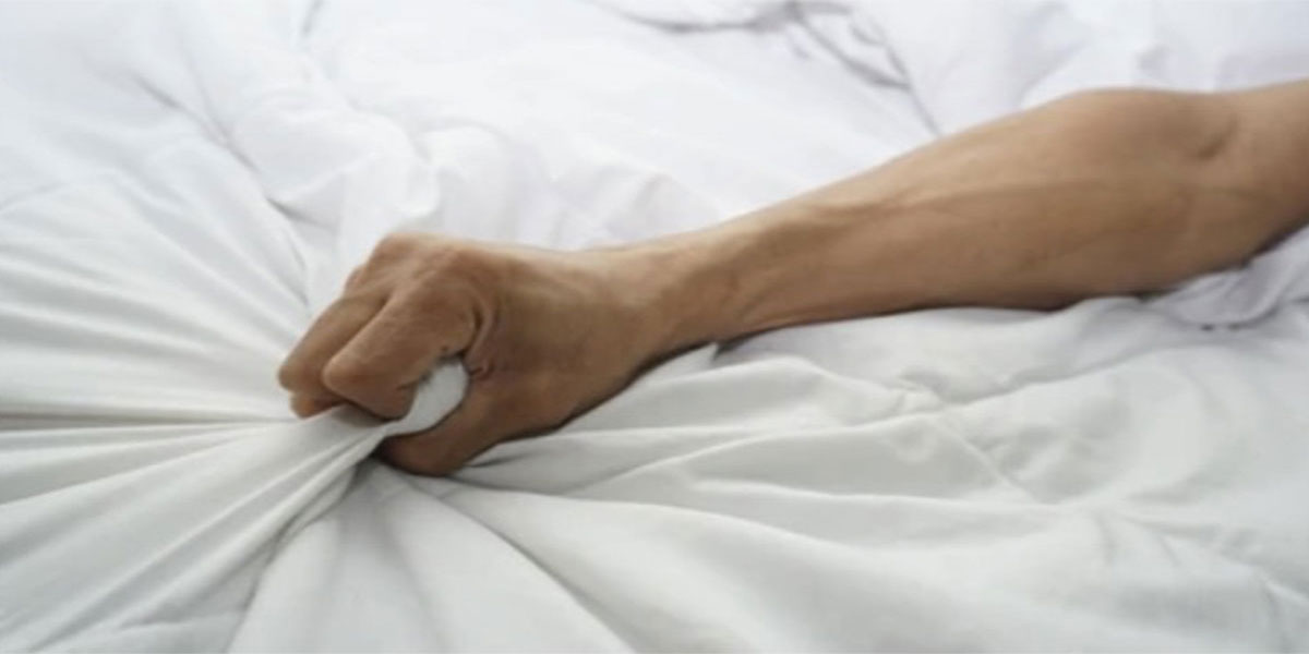main d'un homme qui tire la couverture du lit